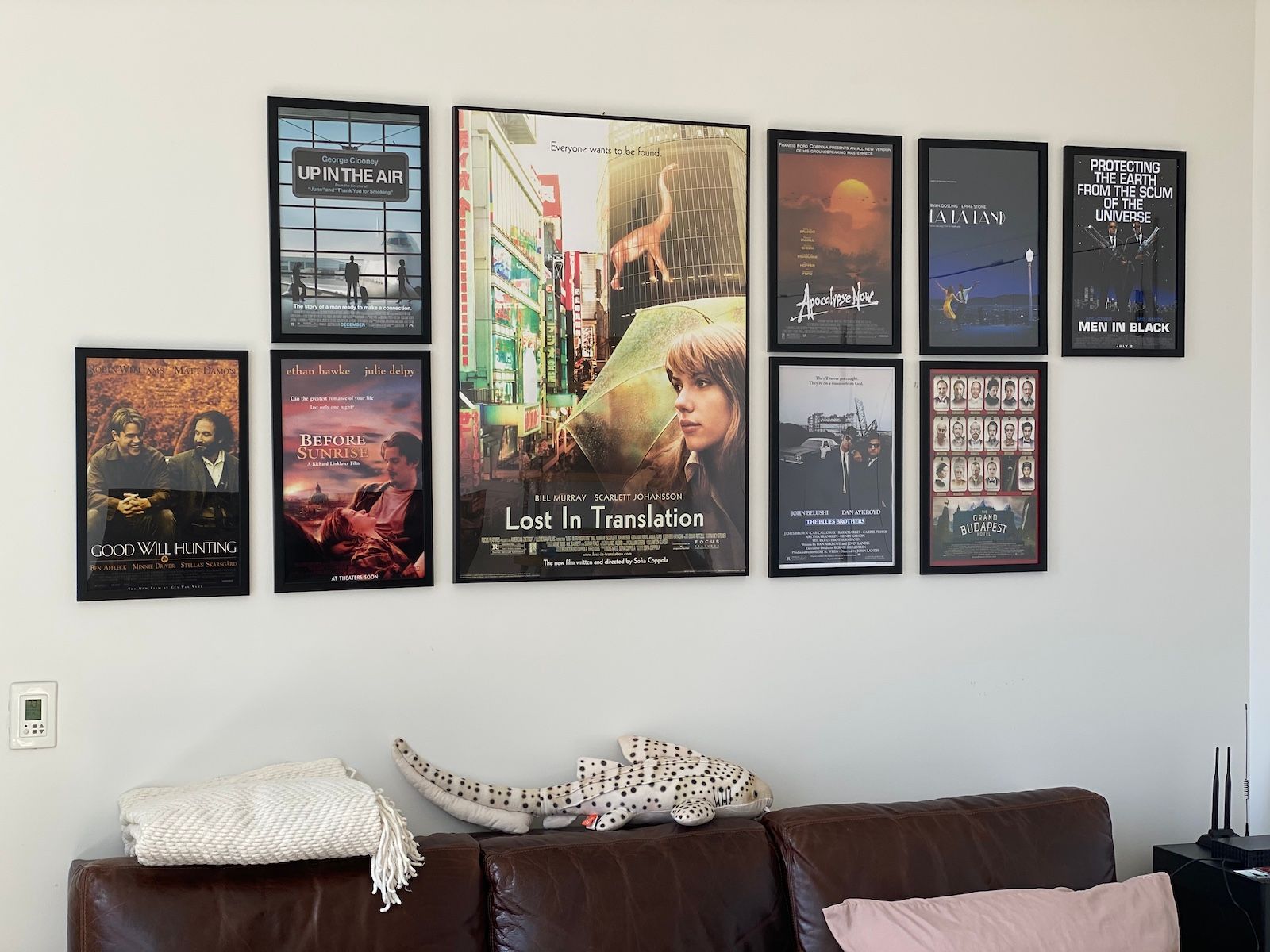 The wall behind my couch with 9 movie posters: Good Will Hunting, Before Sunrise, Up in the Air, Lost in Translation, Apocalypse Now, The Blues Brothers, Grand Budapest Hotel, La La Land, and Men in Black.