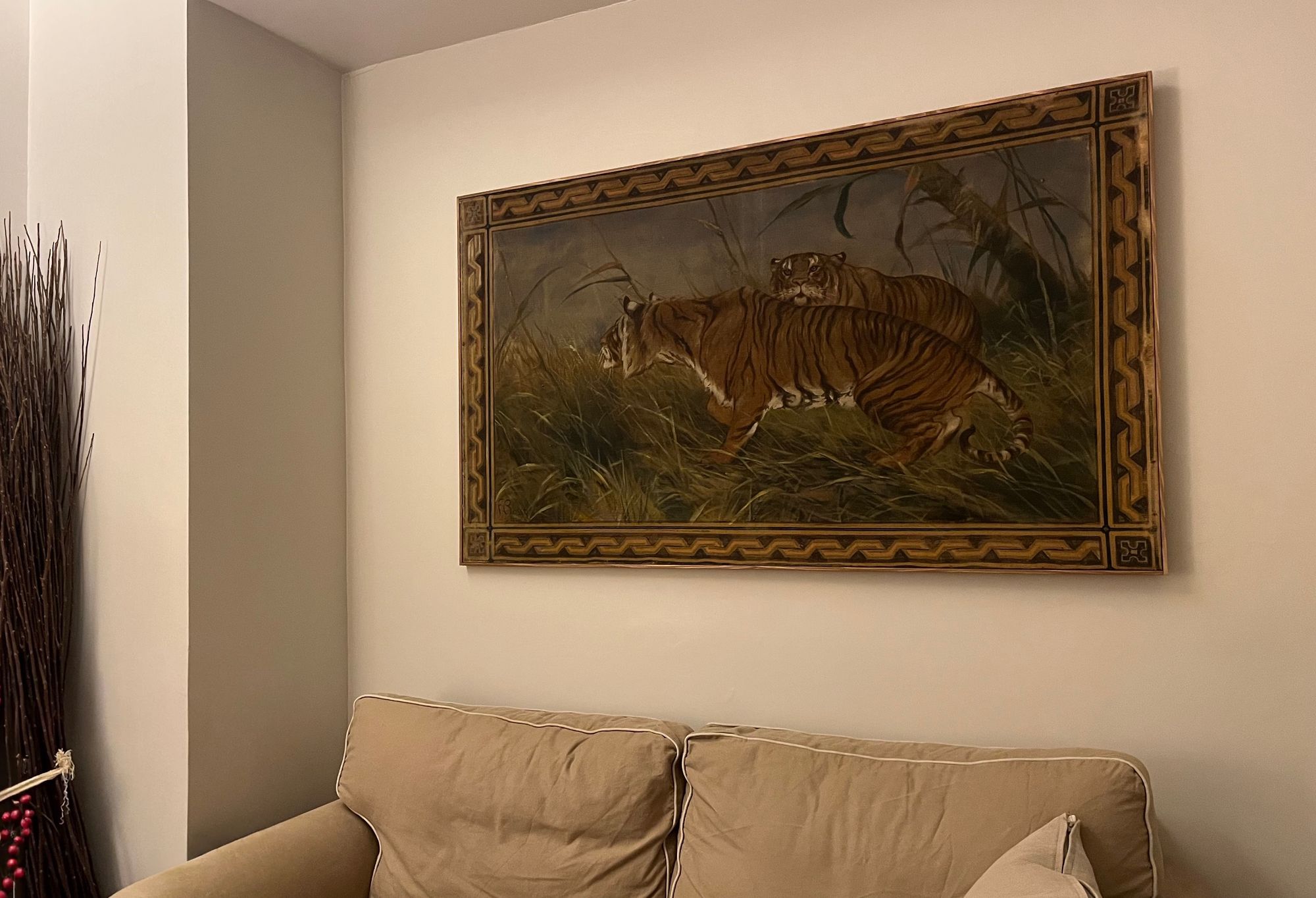 The side of a room, at the bottom there's a sofa, above it a large painting. It shows two tigers in the grass, with a painted frame.